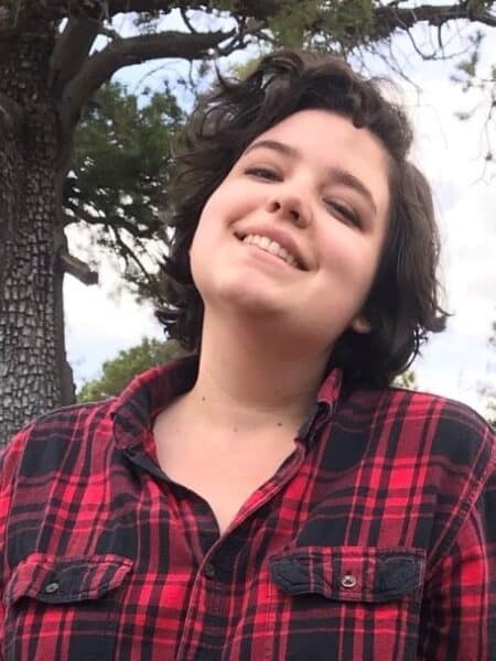 Photo of Tatiana wearing a red and black plaid shirt with a tree in the background