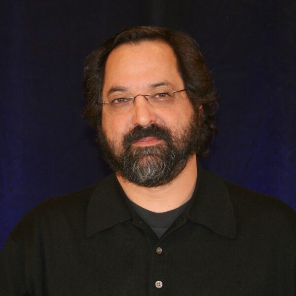 Michael Perlis: white man with dark hair and beard wearing non-rimmed rectangular glasses and a black polo shirt.