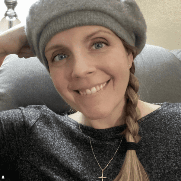 Melly Rosehaven, a woman with blonde braided hair and light blue eyes wearing a black top and gray hat.